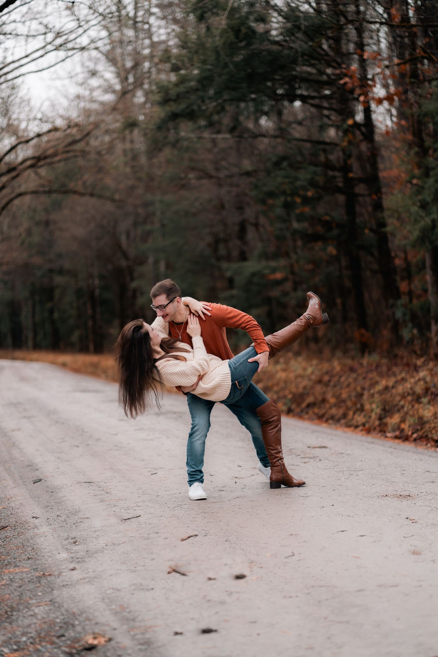 A playful couple dips and poses on a forest path during autumn.