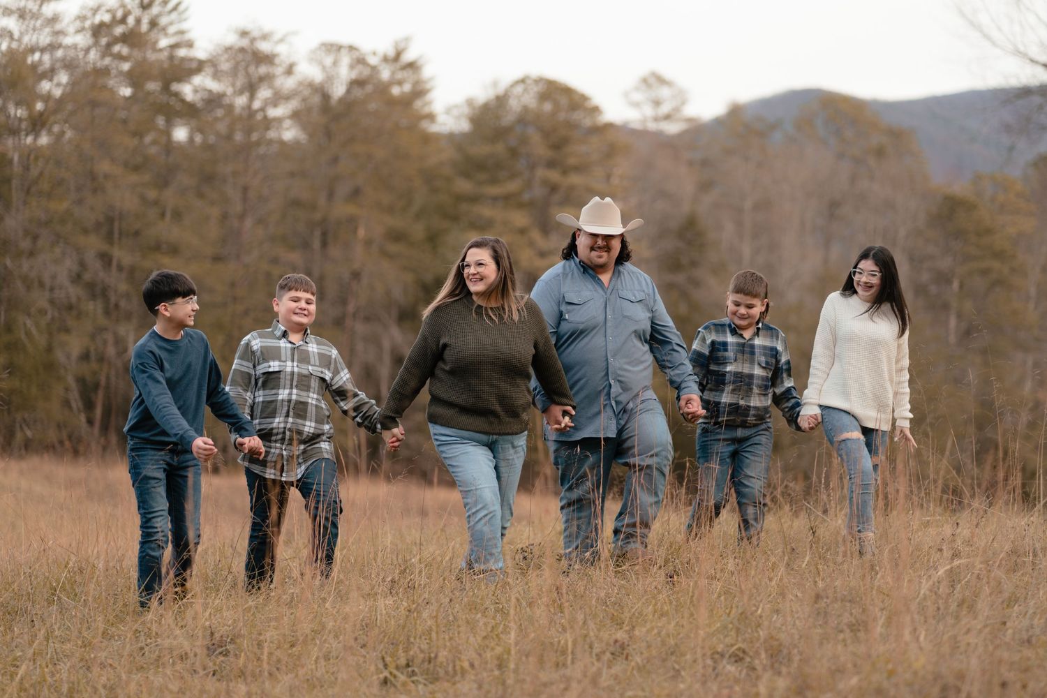 A group walks together through a golden field with mountains visible in the distance.