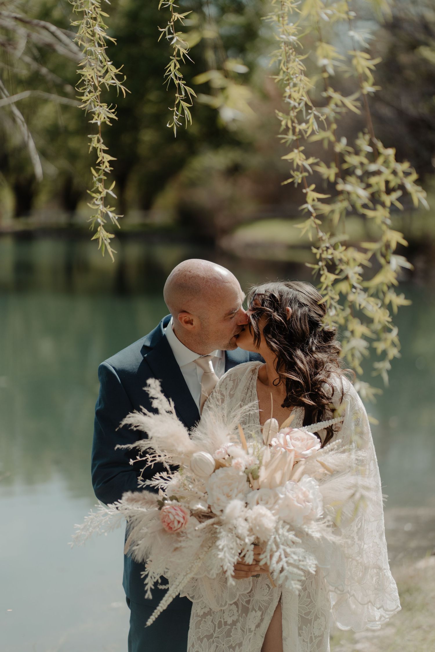 A couple shares an intimate moment with dried flower bouquet by a serene lake.