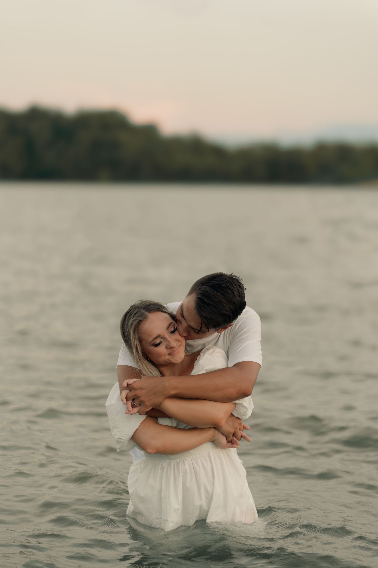 Romantic couple moment in lake waters with misty shoreline at dusk.