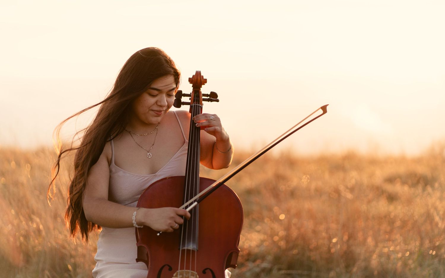 Cellist playing in a golden sunset field wearing a light colored dress.