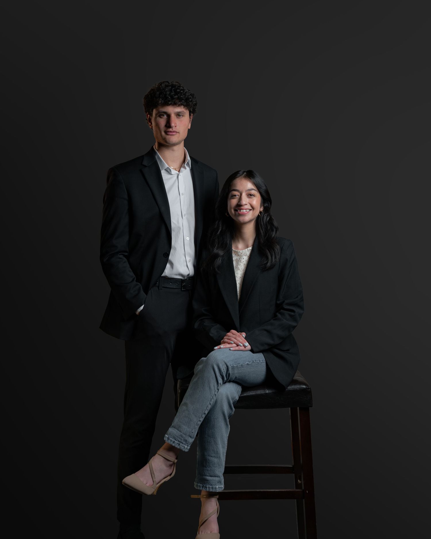 A formal studio portrait of a couple in business attire against a dark background.
