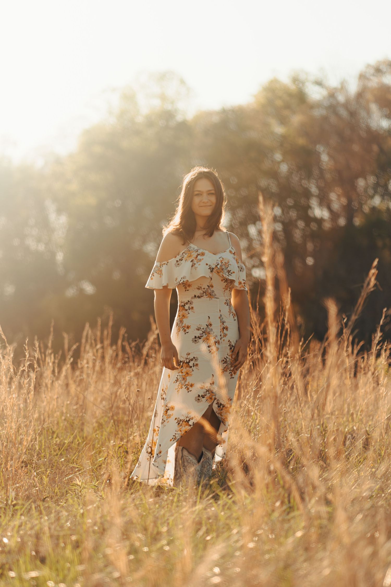 Woman in floral dress standing in golden sunlit field at sunset.