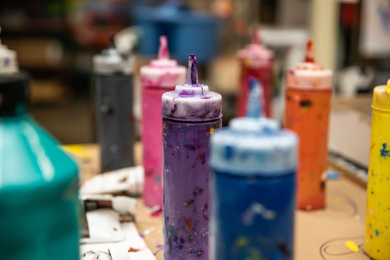 Colorful paint squeeze bottles on a table in an art studio, with purple bottle in focus.