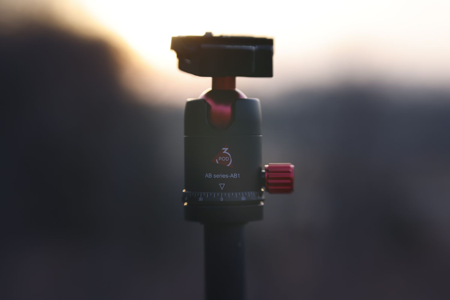 Close-up of a Manfrotto ball head tripod mount against a blurred sunset background.
