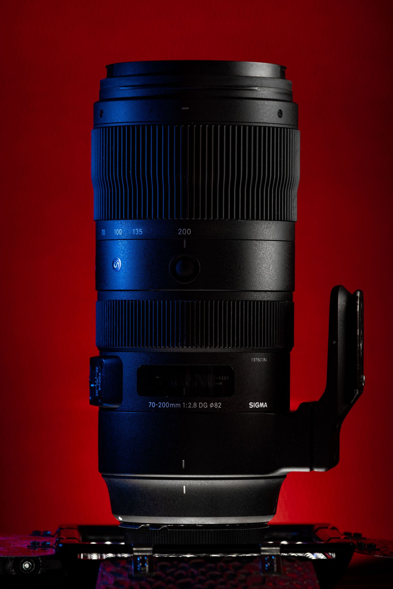 Sigma 70-200mm f/2.8 DG DN telephoto zoom lens standing upright on a tripod collar against a red background.