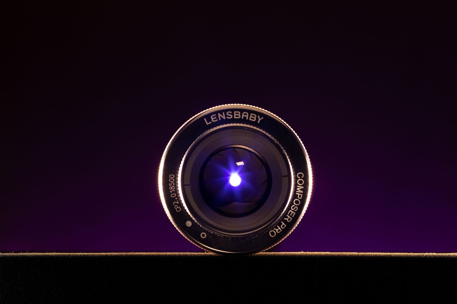 Close-up of a Lensbaby camera lens with a blue light reflection on a dark purple background.