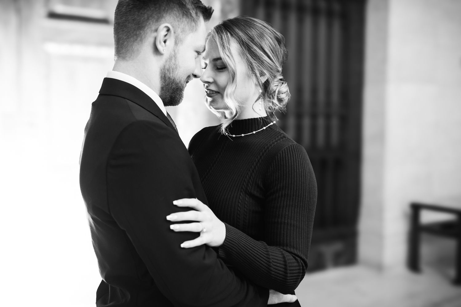 Black and white photo of a romantic couple embracing and smiling at each other in elegant attire.