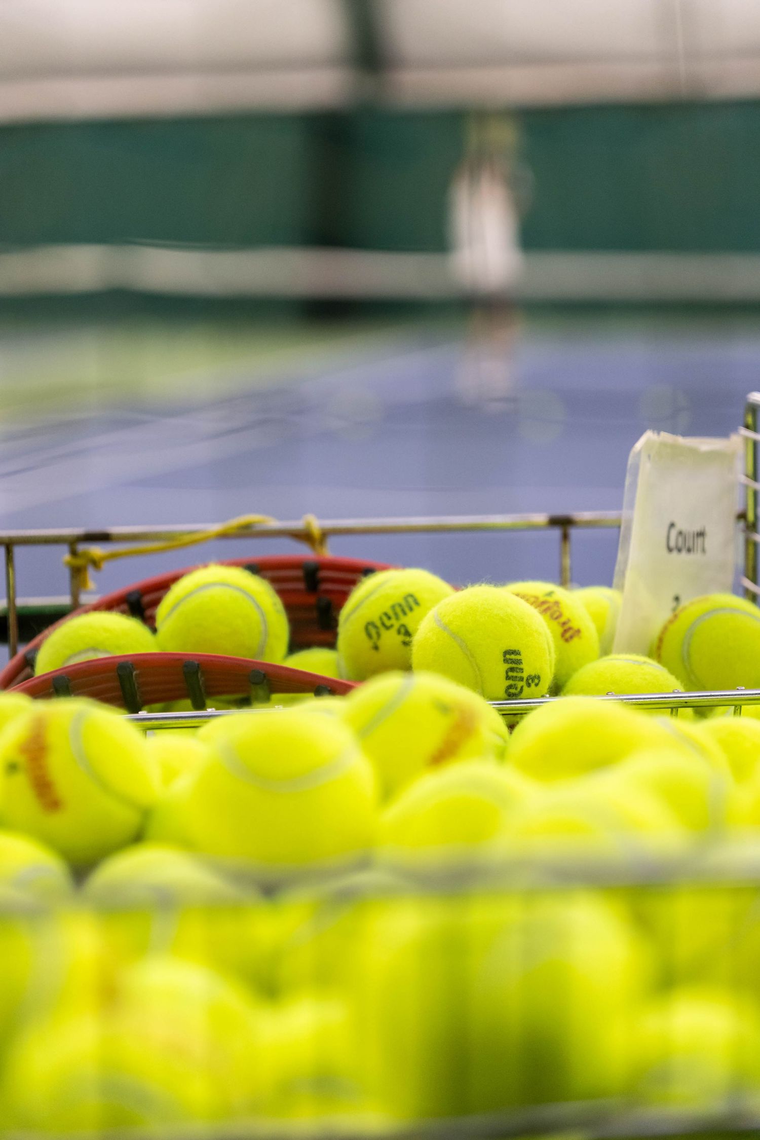 Bright yellow Penn tennis balls piled in a wire basket on a blue tennis court.