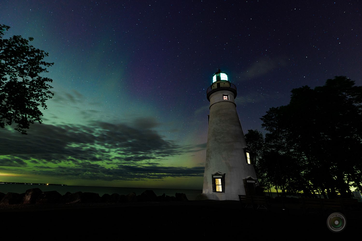 Lighthouse glowing at night with vibrant aurora borealis illuminating the sky in green and blue hues.