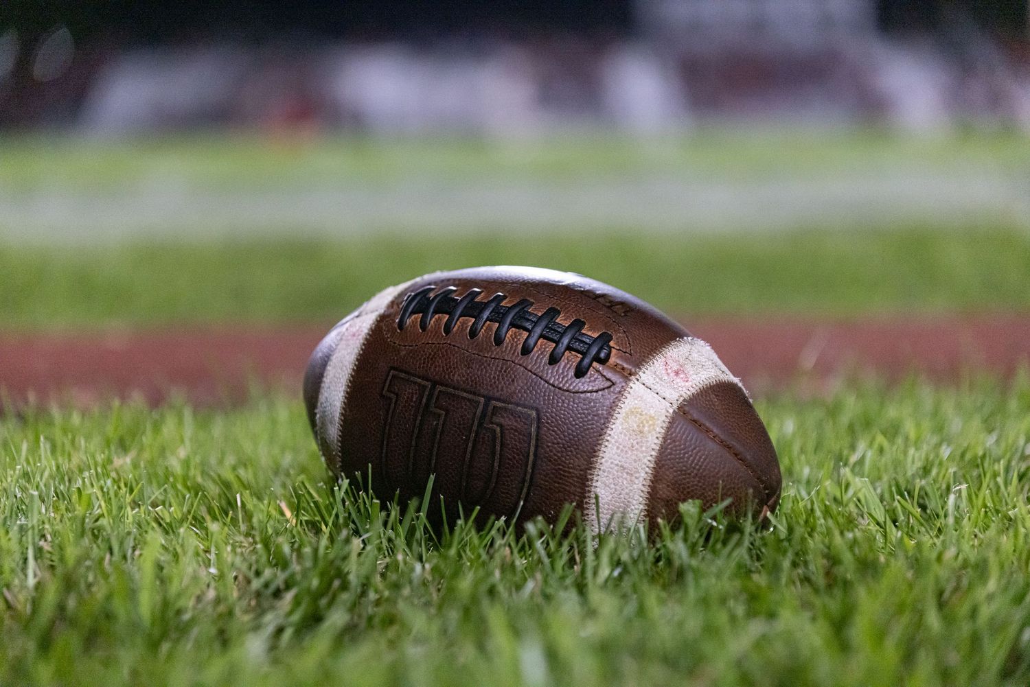 Close-up of a brown leather American football resting on green grass on a football field.