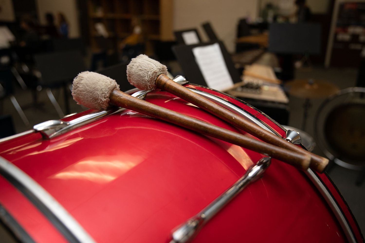 Two drumsticks resting on a red snare drum in a music room setting.