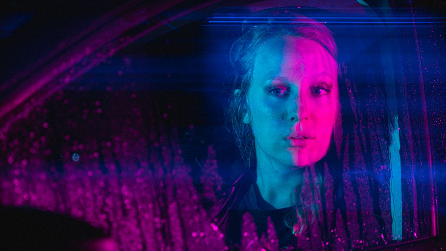 Woman with wet hair illuminated by vivid pink and blue neon lights, creating a dramatic cinematic atmosphere.