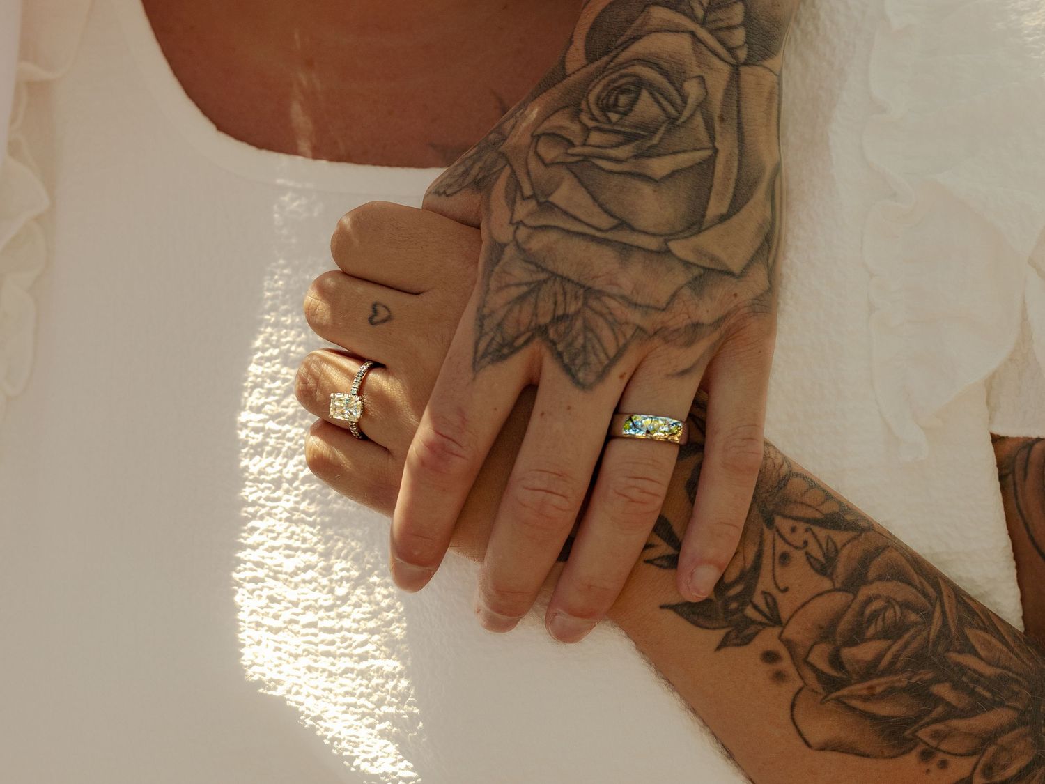 Two hands with wedding rings intertwined, one adorned with rose tattoos, symbolizing love and commitment.