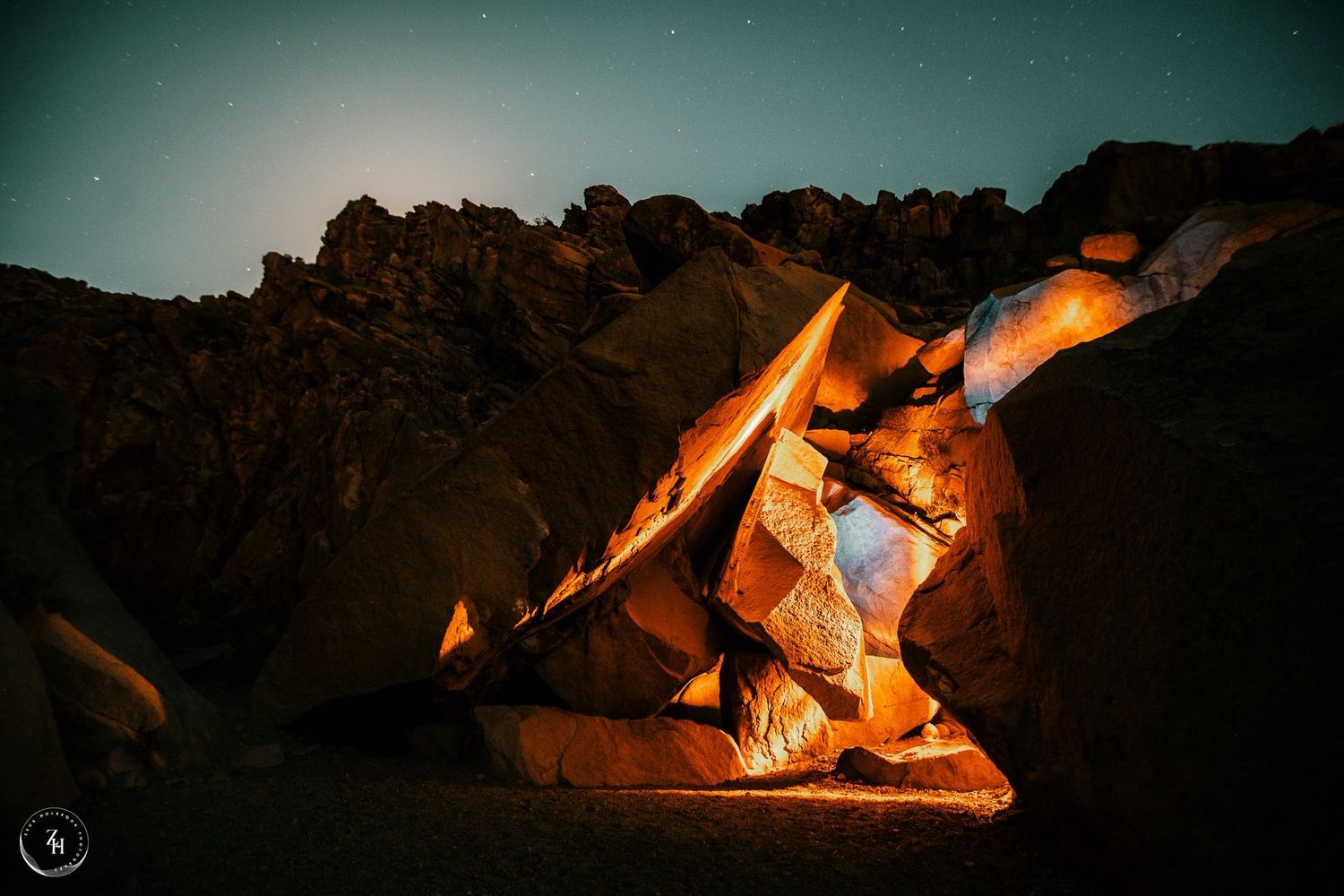 Illuminated rock formation glowing orange under a starry night sky in a desert landscape.