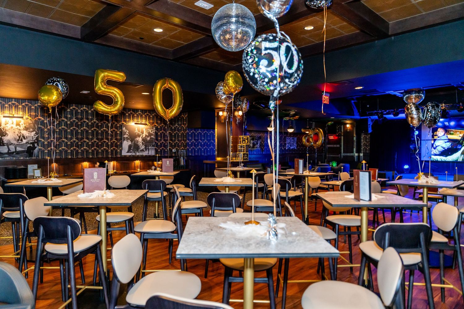 Restaurant decorated for a 50th birthday party with gold balloons, disco balls, and elegant table settings.