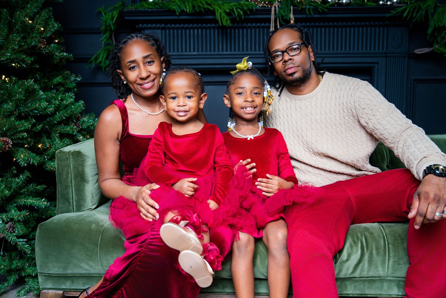 Family of four in red outfits posing for a festive Christmas portrait on a green velvet sofa.