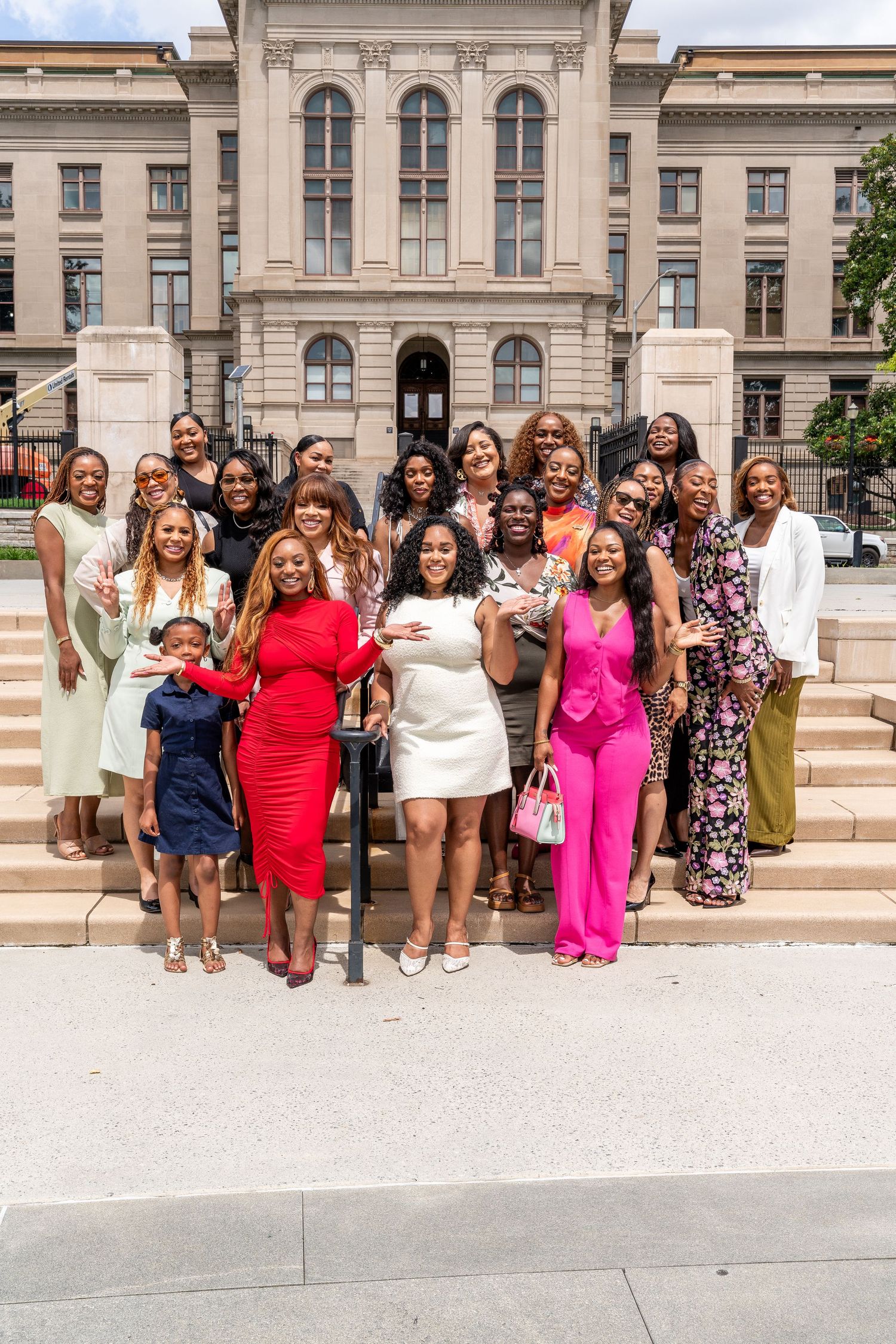 A large group of well-dressed women posing on steps in front of a grand government building on a sunny day.