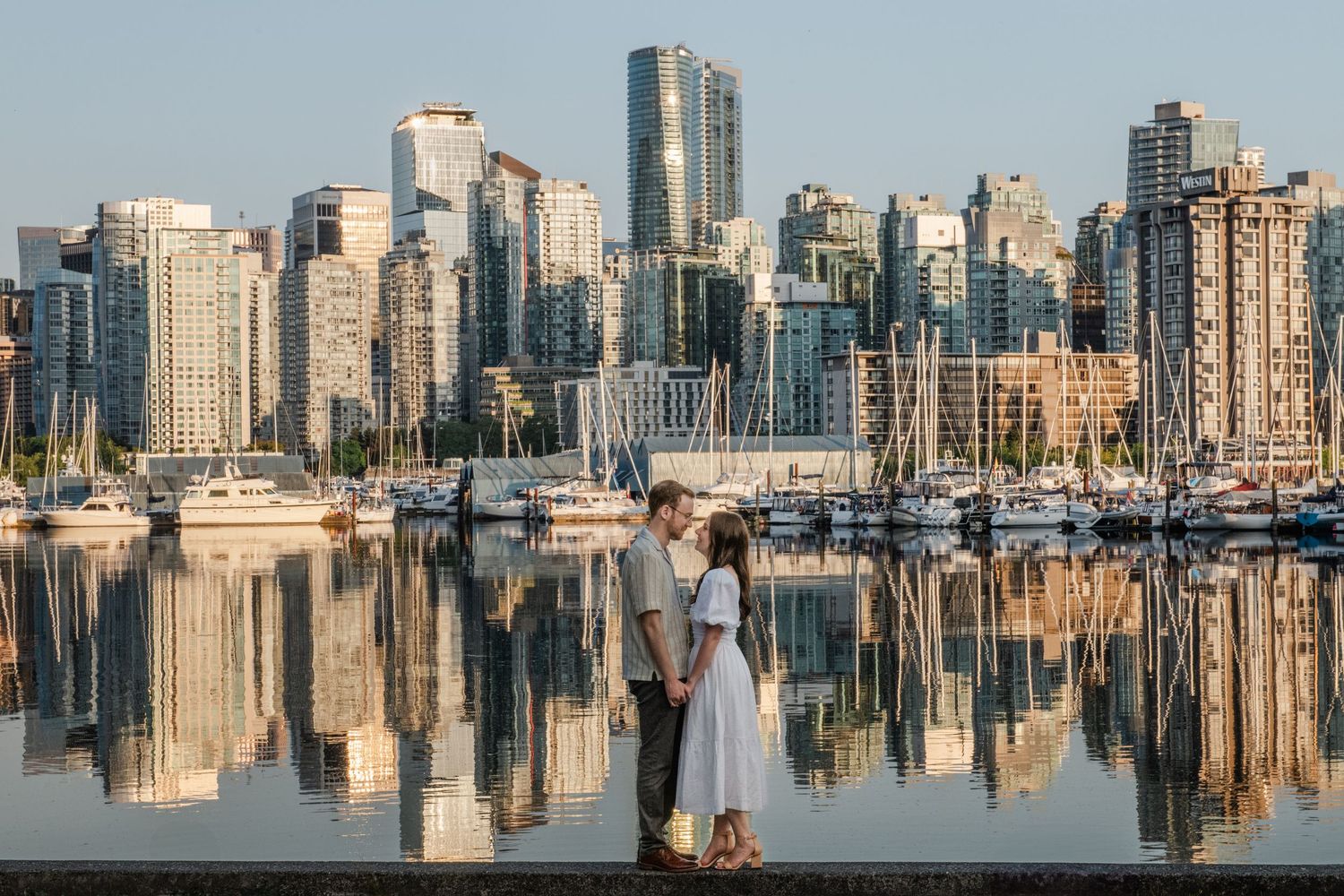 Vancouver skyline reflects in calm harbor waters with boats docked at Coal Harbour marina during sunset.