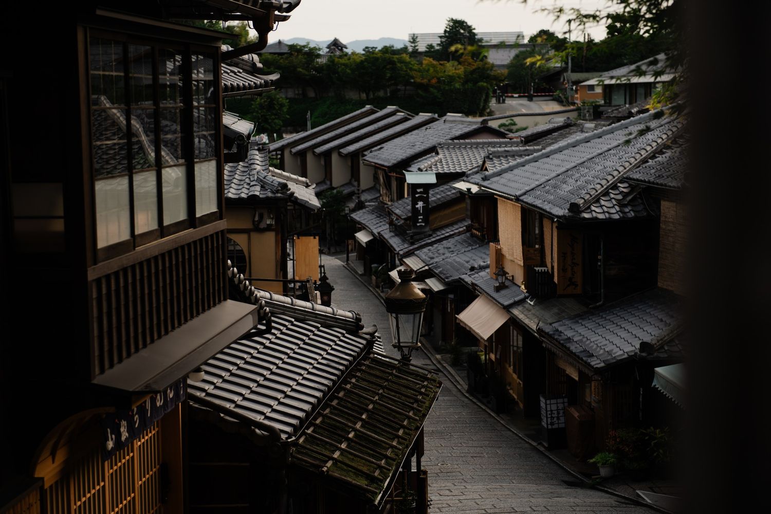 Traditional Japanese houses with sloping tiled roofs line a narrow street at dusk in a historic neighborhood.
