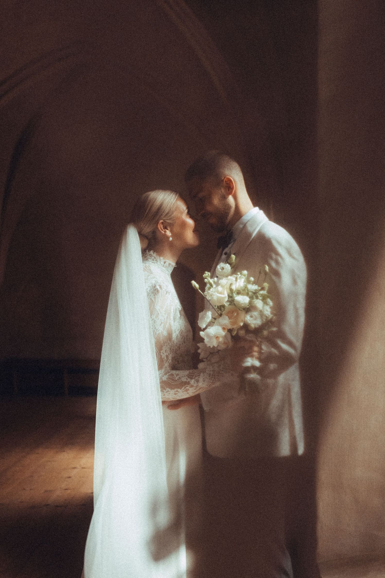 Couple shares an intimate moment in soft lighting while holding white flowers.