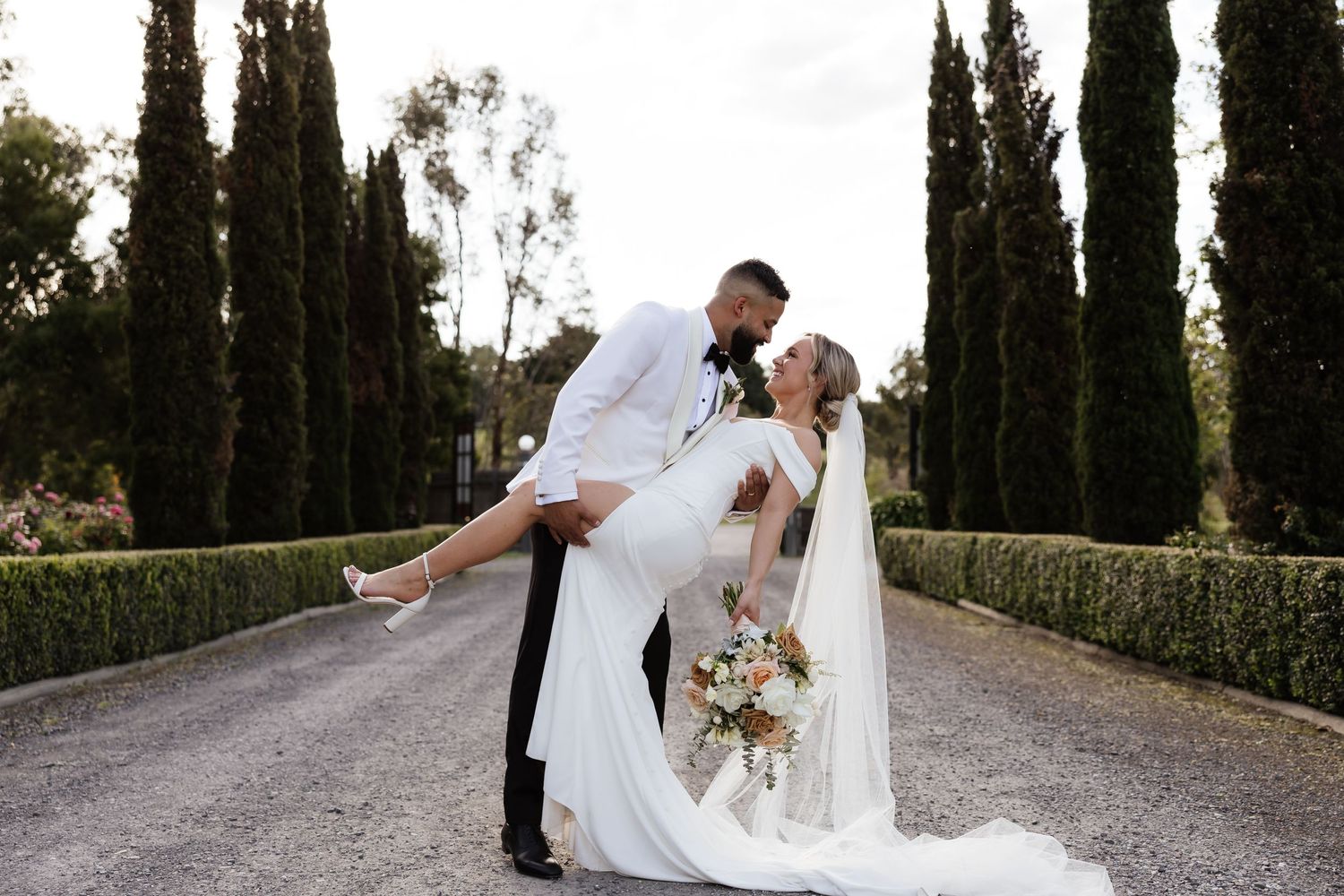 Romantic couple poses among cypress trees in elegant wedding attire.