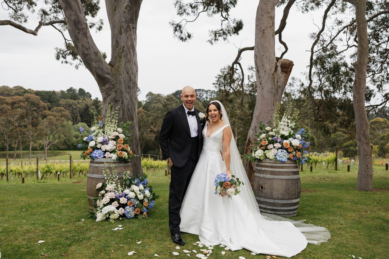 Fun wedding couple beneath towering eucalyptus trees in a rustic outdoor setting with floral arrangements at Polperro Winery Wedding