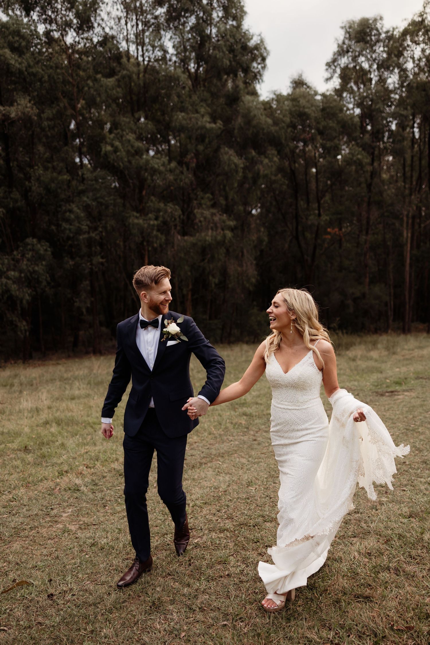 Newlyweds run and laugh together in a rustic outdoor setting.