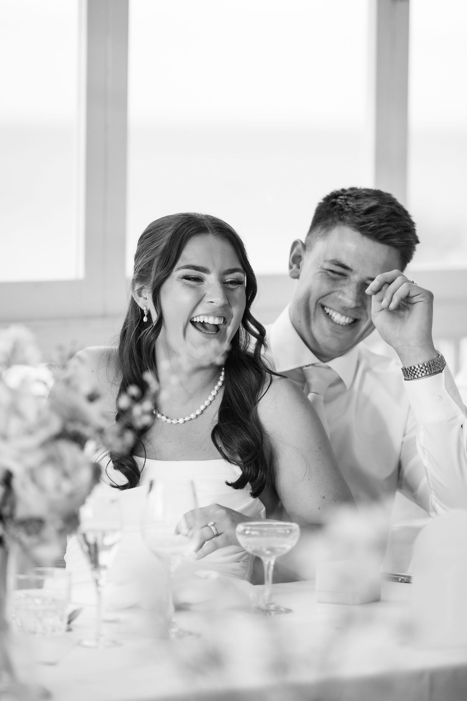 A joyful couple shares a candid laughing moment together at a wedding reception table.