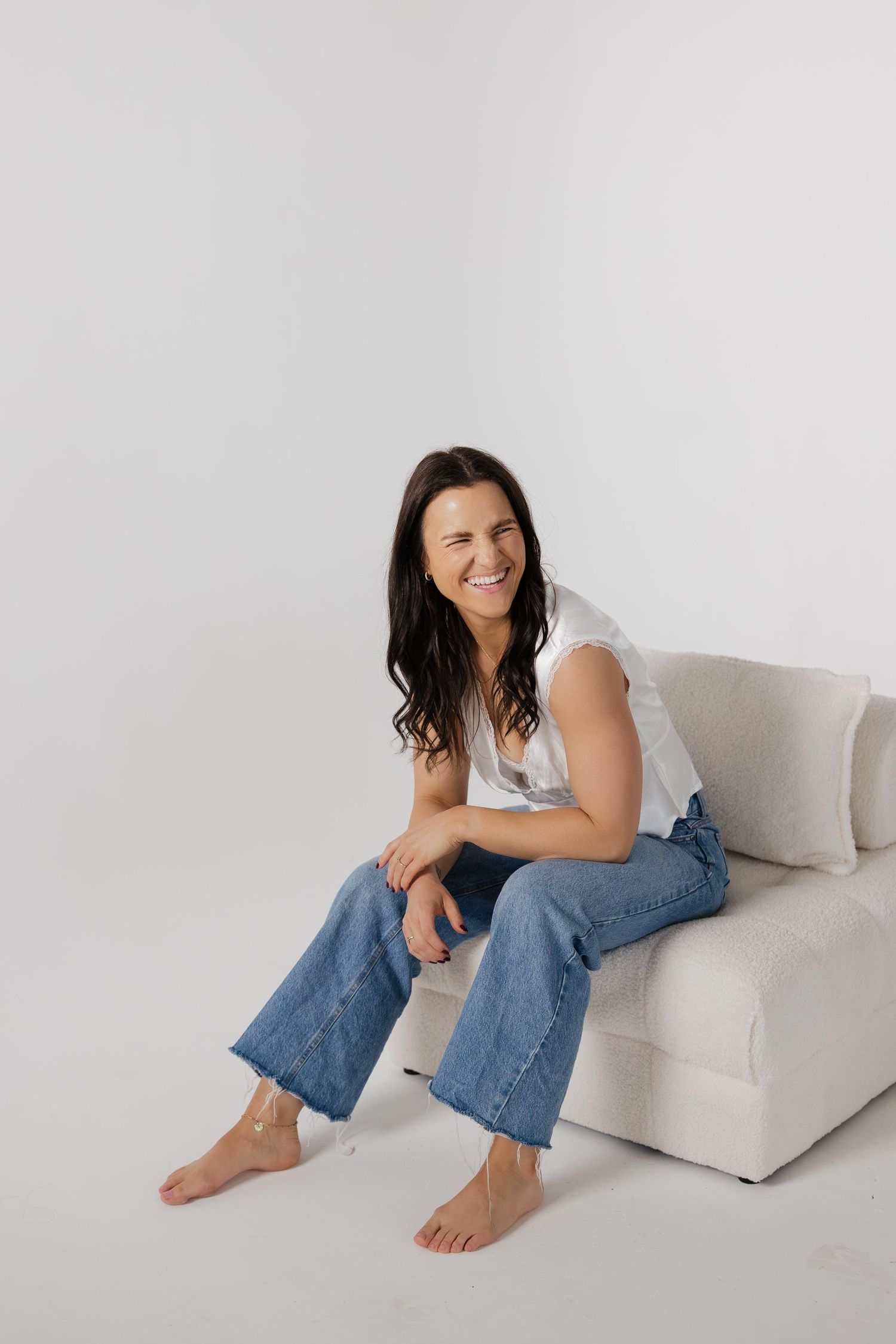 Four photos showing someone in blue jeans and a white top reclining on a light colored couch against a white backdrop.