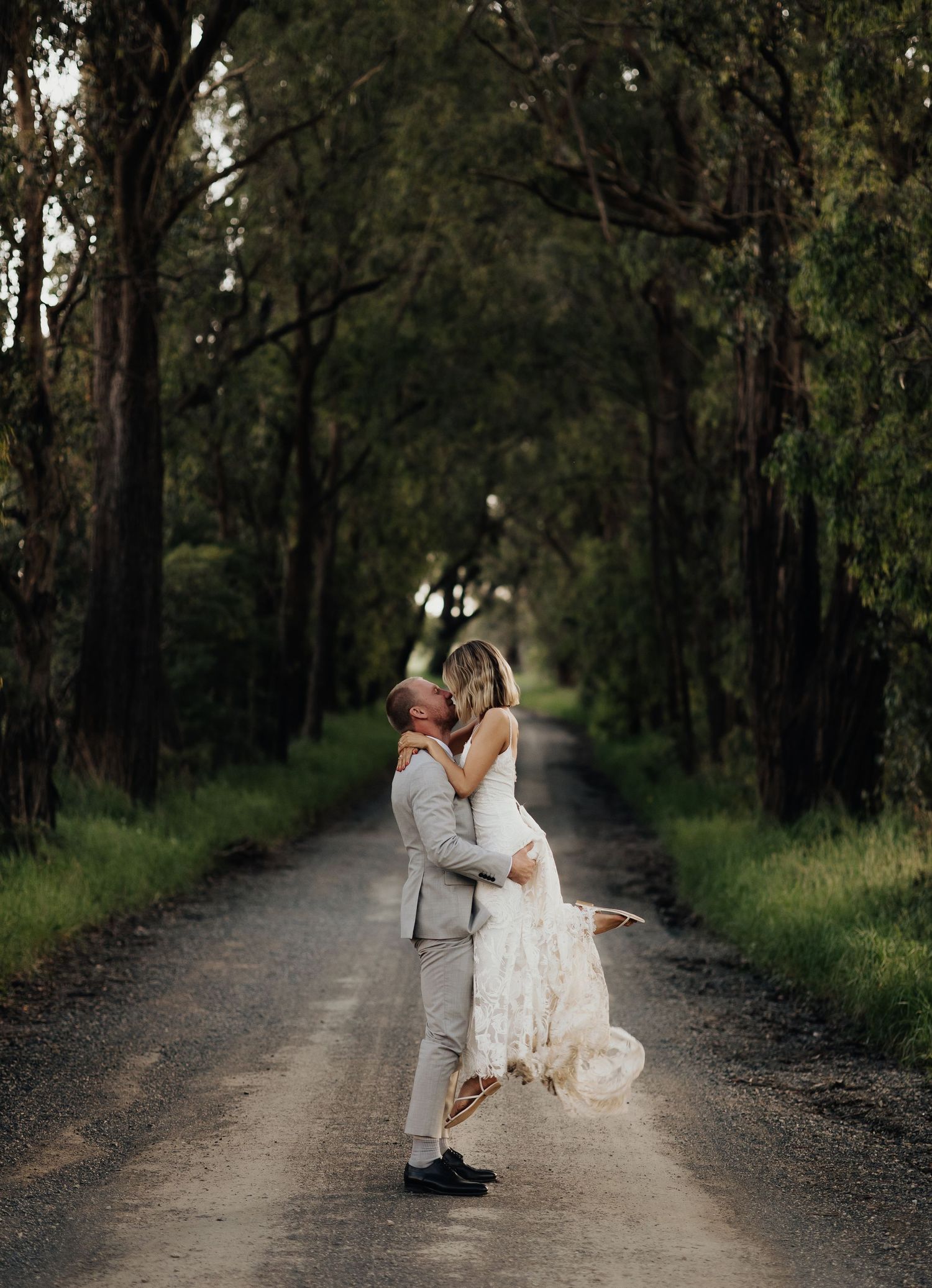 Romantic wedding couple embraces on a tree-lined dirt road.