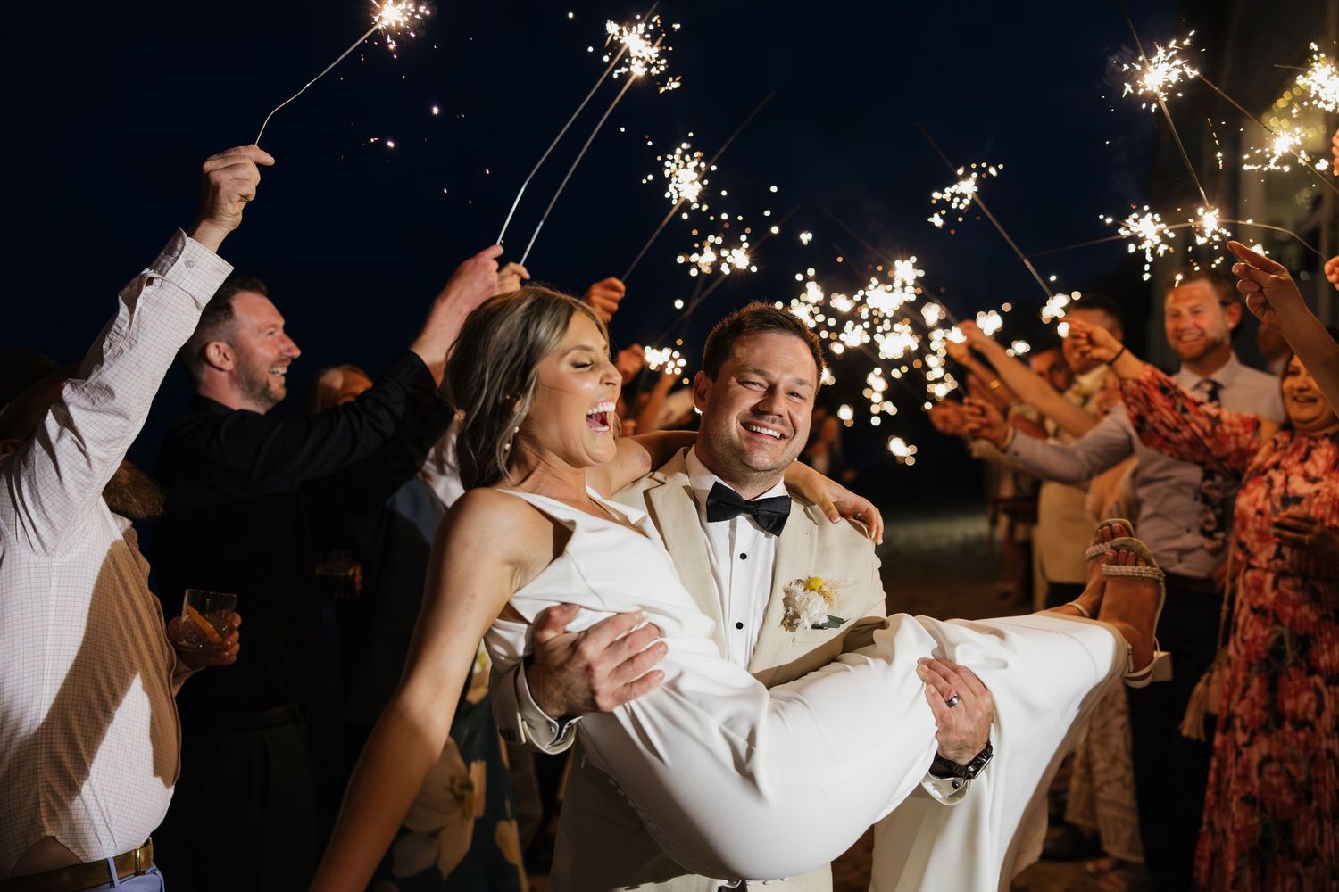 Bride and groom sparkler exit at night wedding celebration with guests holding sparklers.