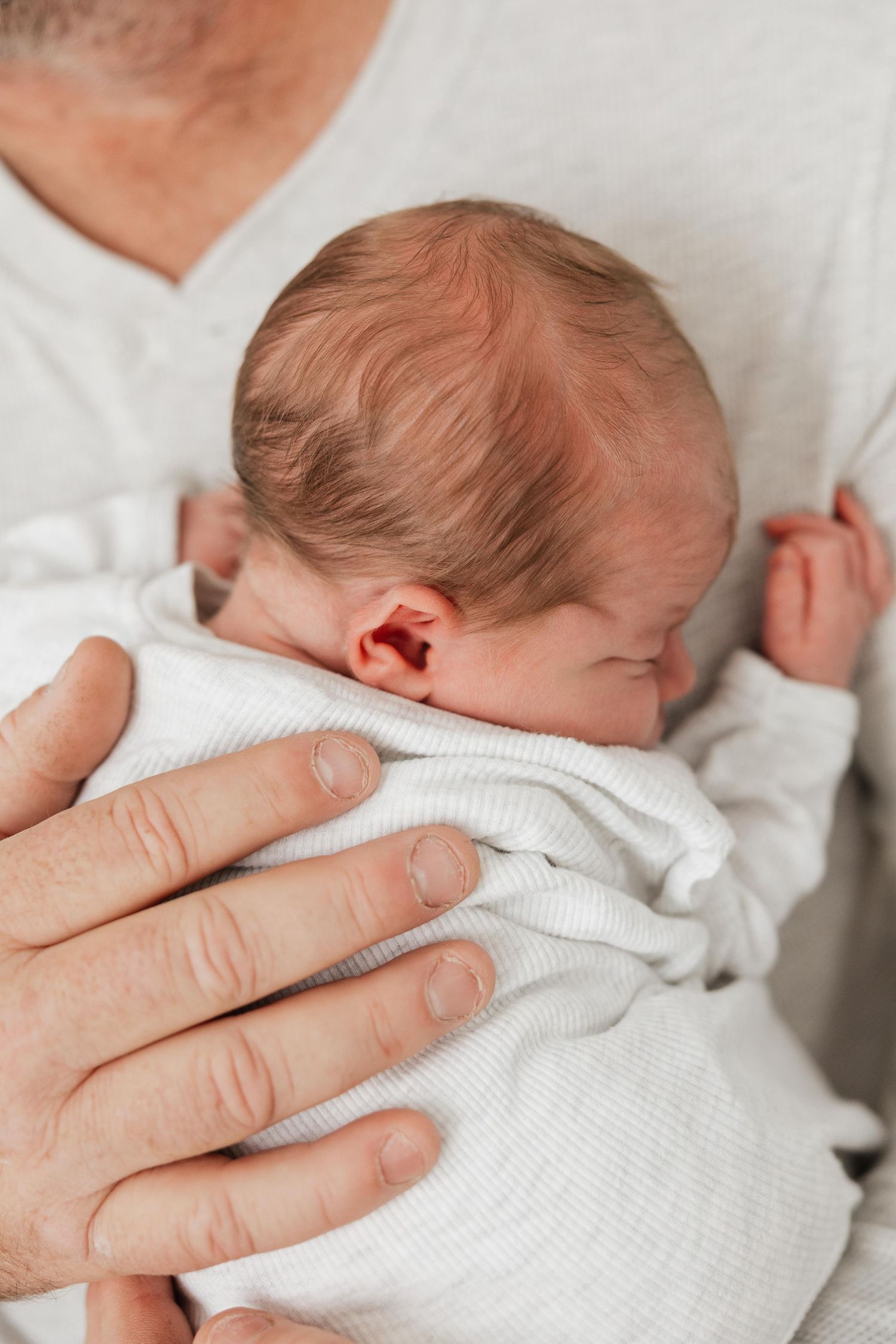 Adult hand tenderly holds small baby swaddled in soft white blanket, showing tender nurturing touch.