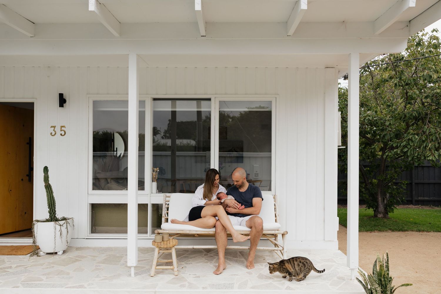 Couple relaxing on a white bench on a modern home porch with a cat nearby.