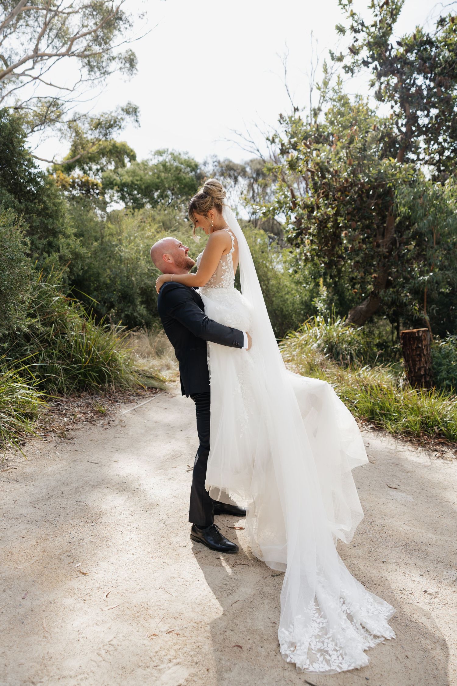 A couple sharing an intimate moment on a dirt path surrounded by lush greenery on their wedding day.