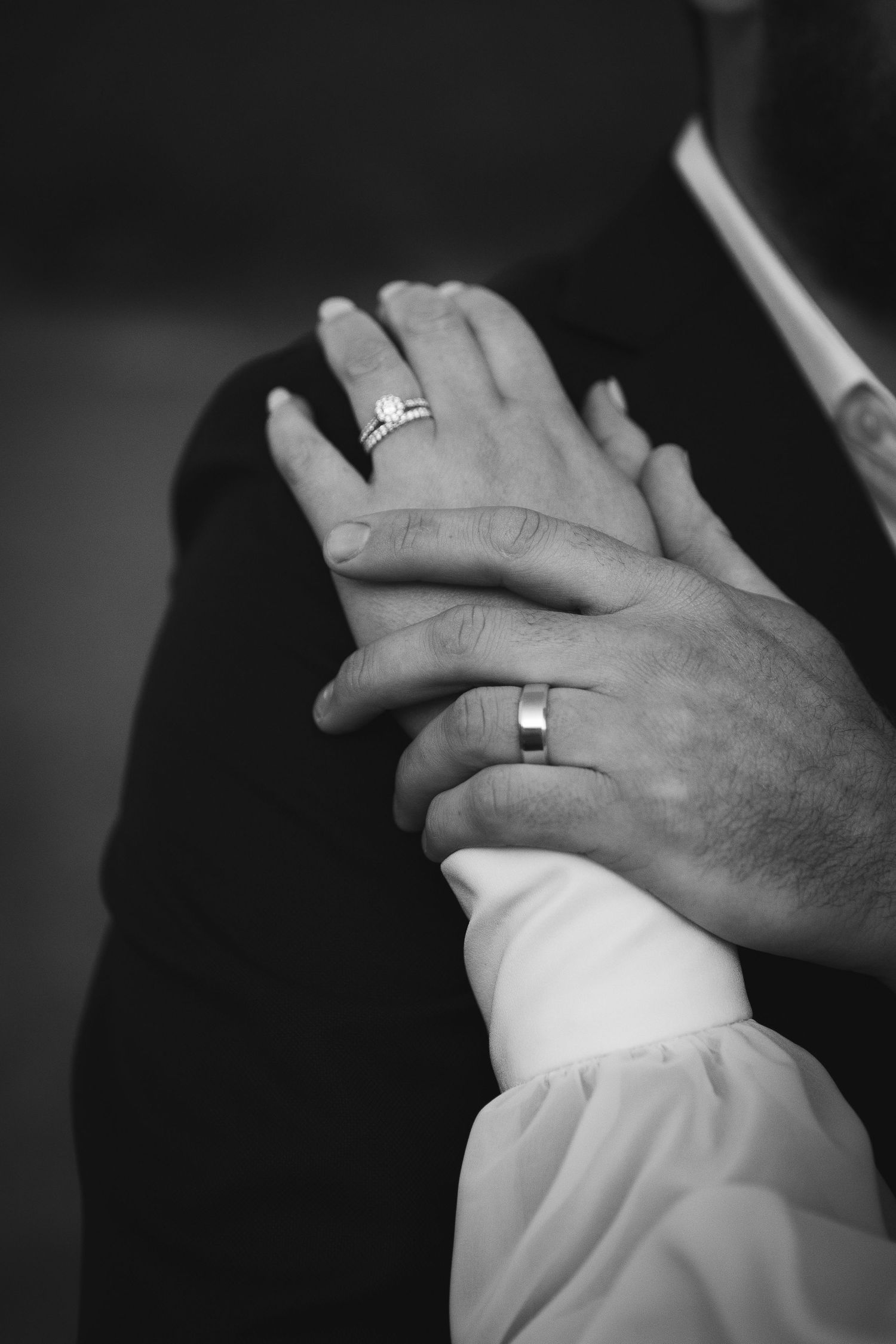 Black and white close-up of two hands with wedding rings touching tenderly in an intimate moment.