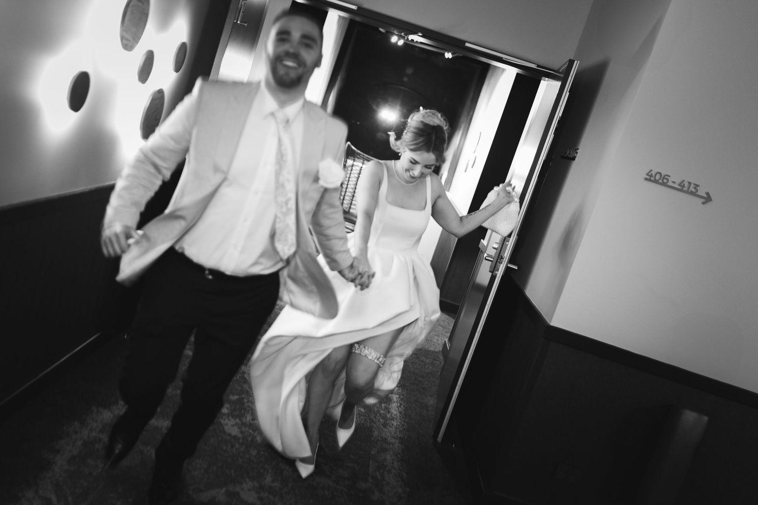 A playful black and white photo of newlyweds running through a hallway.