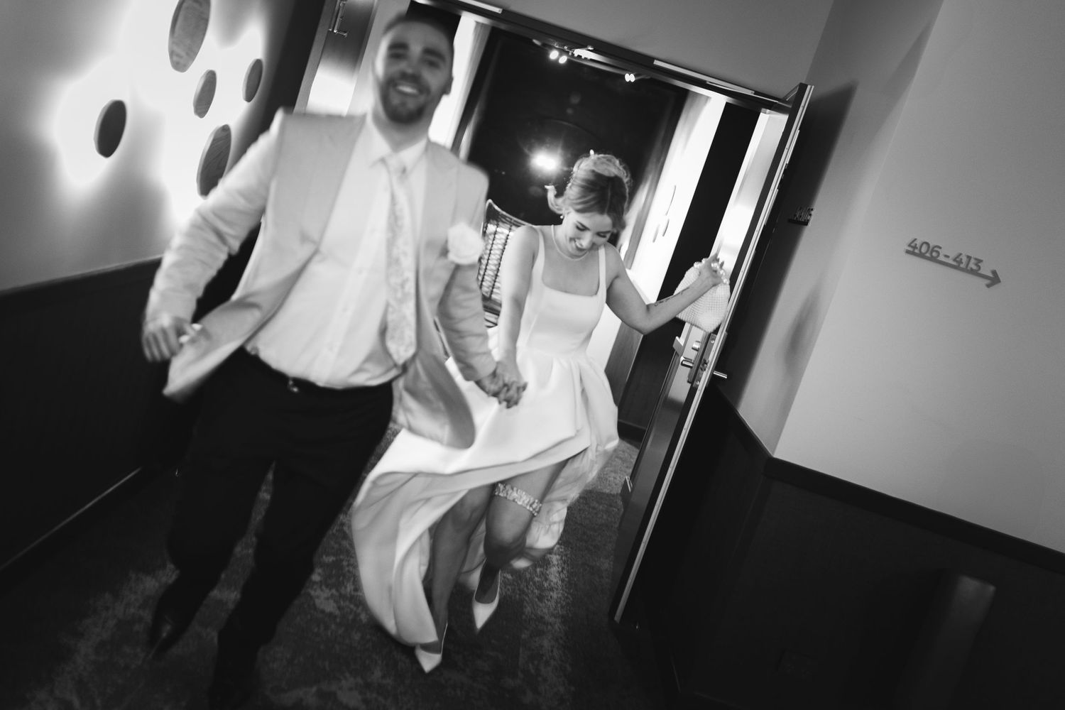 Black and white photo of newlyweds running through hallway after ceremony.