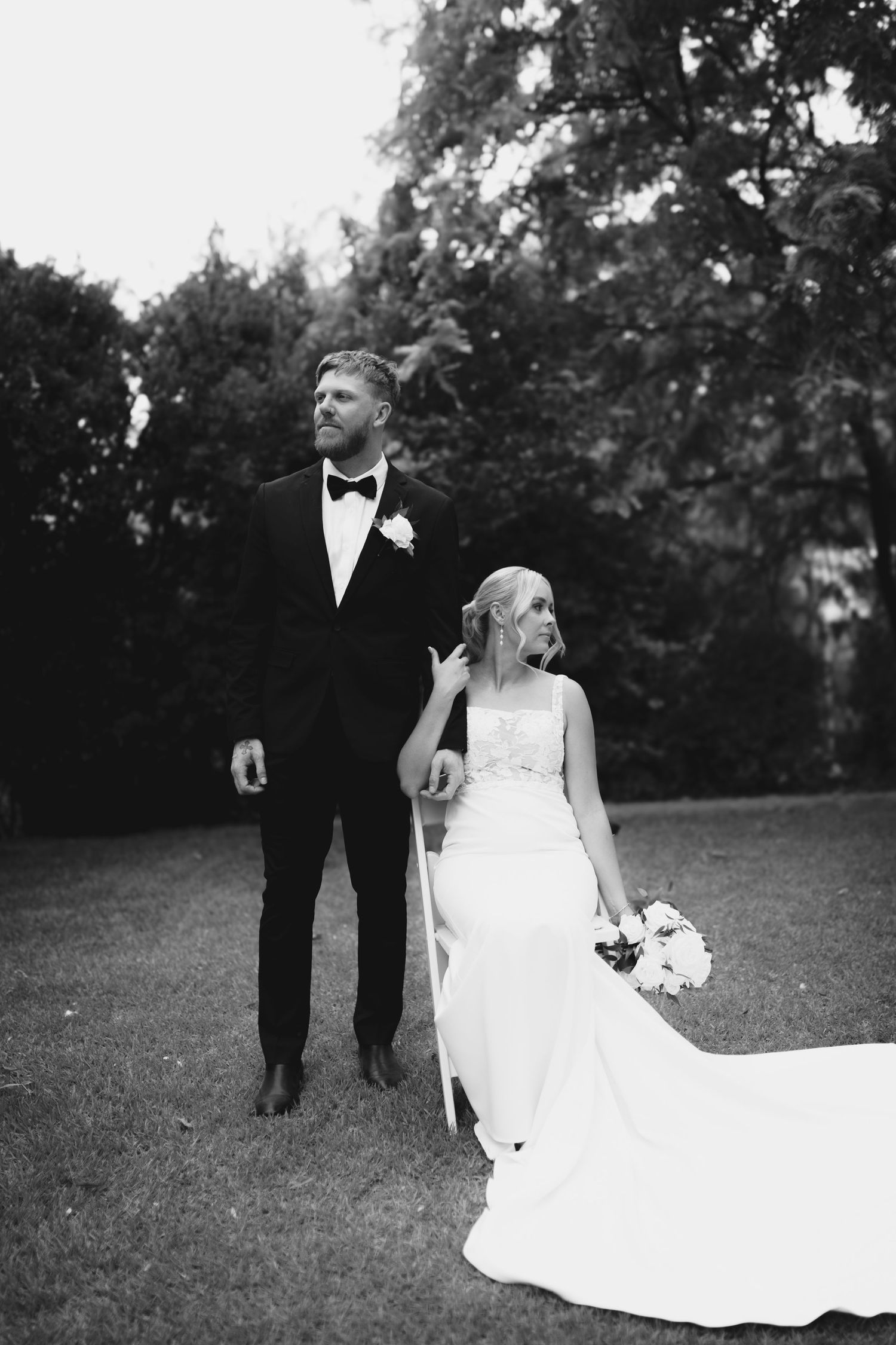 Black and white portrait of a bride and groom standing together on a grassy lawn.