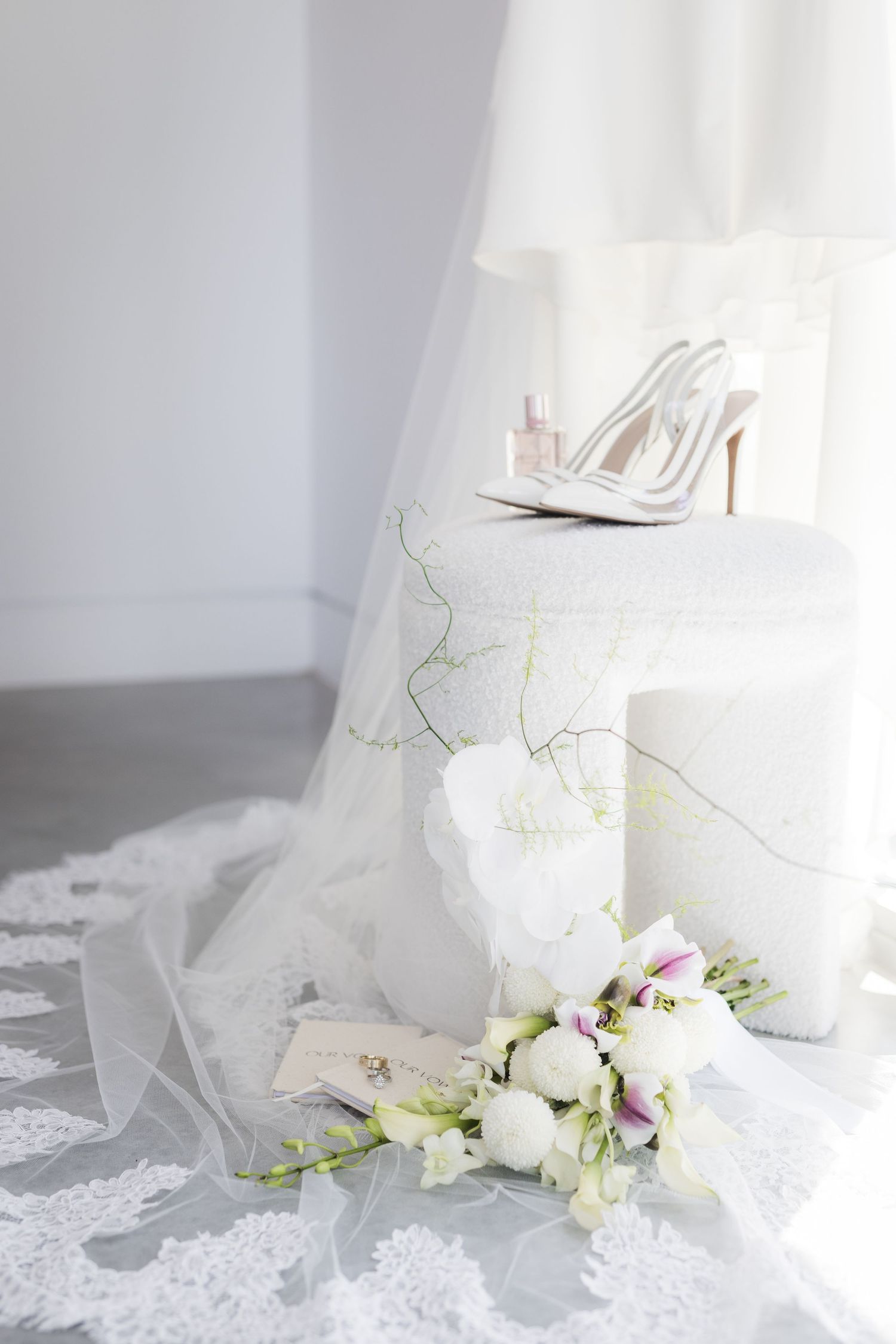 White bridal high heels with floral decor and veil on light backdrop create an elegant wedding composition.