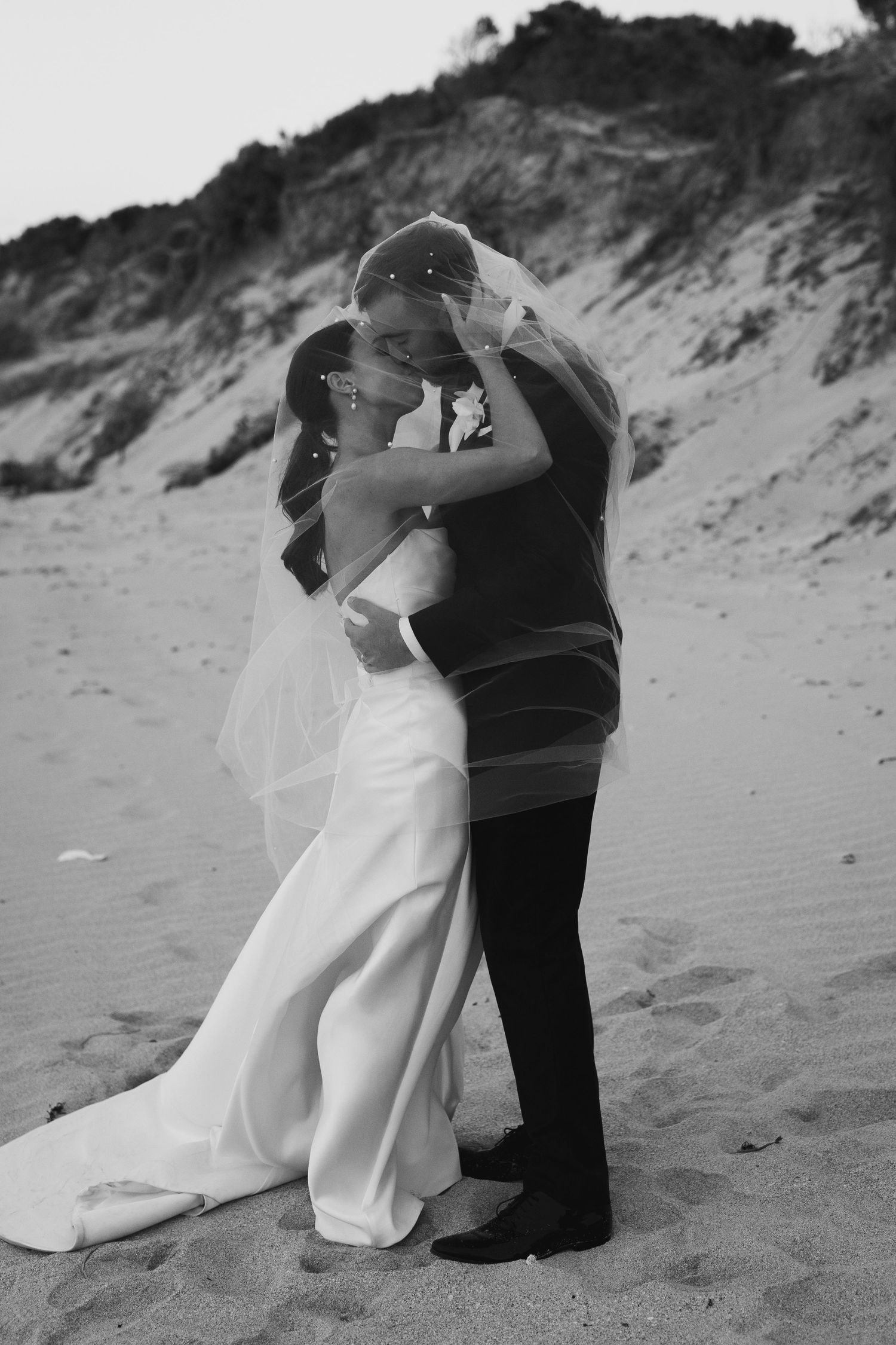 A romantic embrace between newlyweds on a sandy beach at sunset.