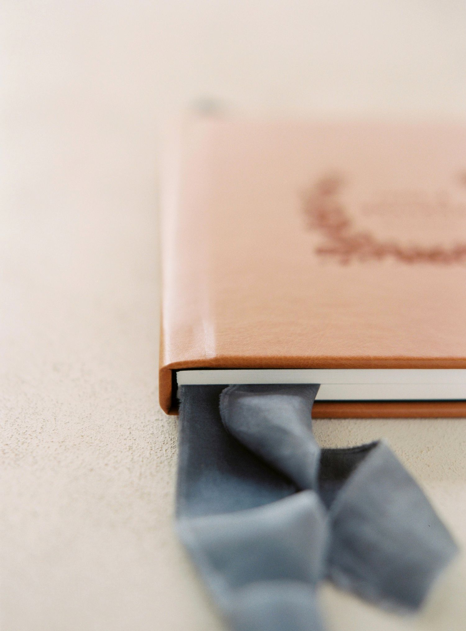 A luxury leather-bound book with a soft gray silk ribbon bookmark against a neutral beige background.
