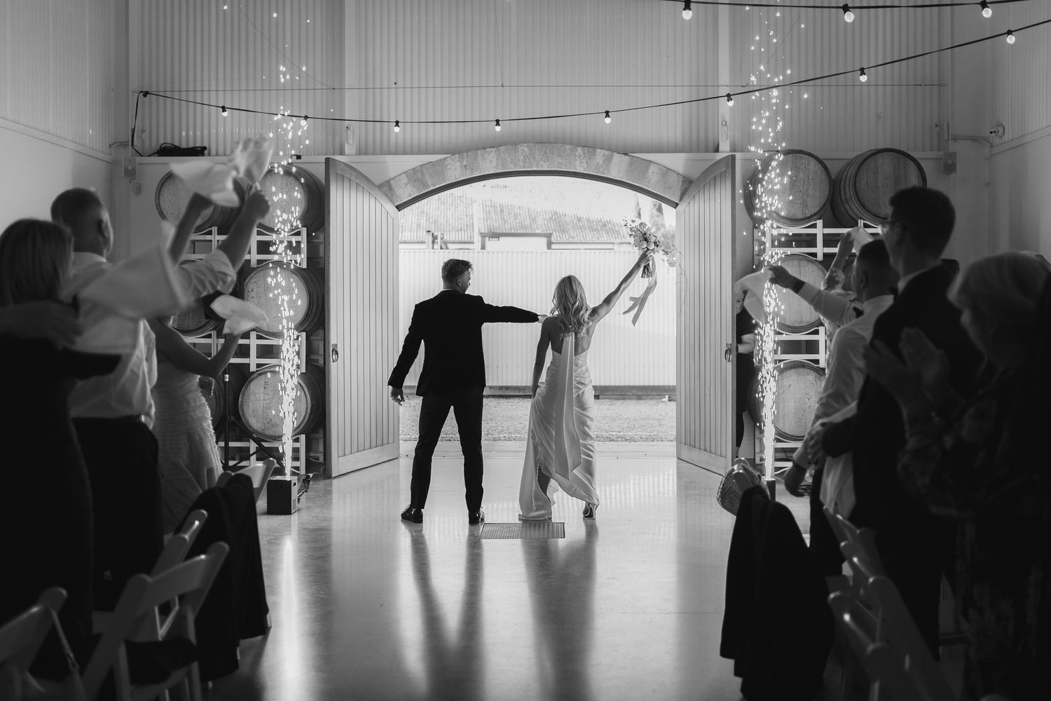 A black and white photo of a couple making their grand wedding exit through a tunnel of sparklers and guests.