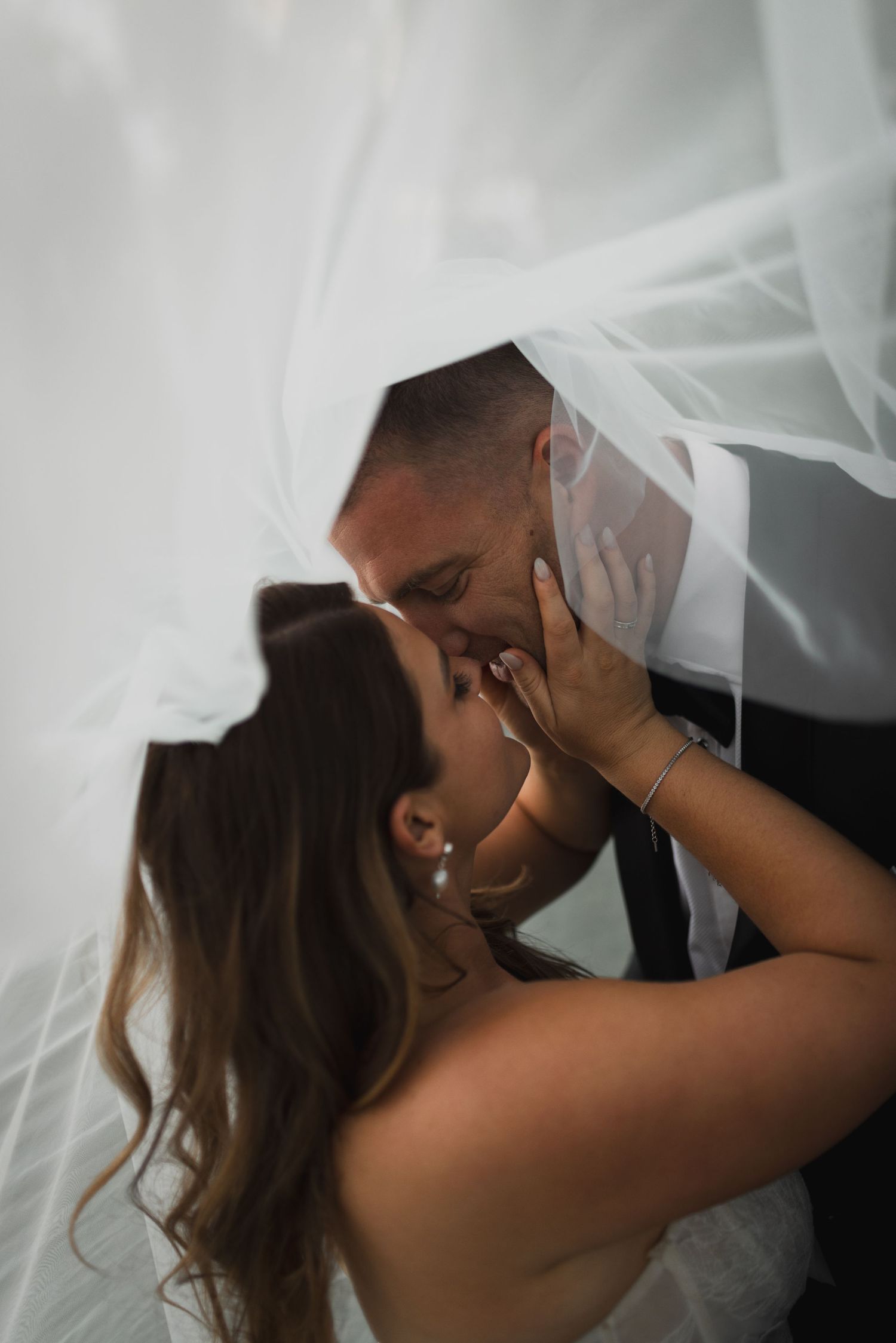 Romantic moment under a flowing white veil during a wedding ceremony.