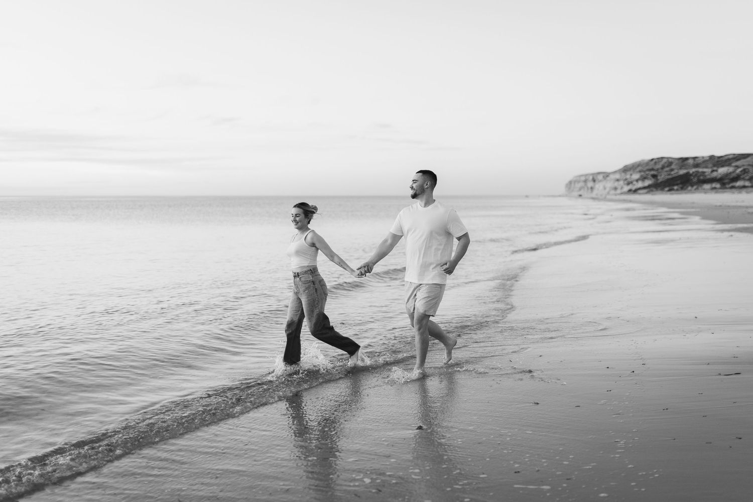 Black and white photo of two people walking along the shoreline at the beach.