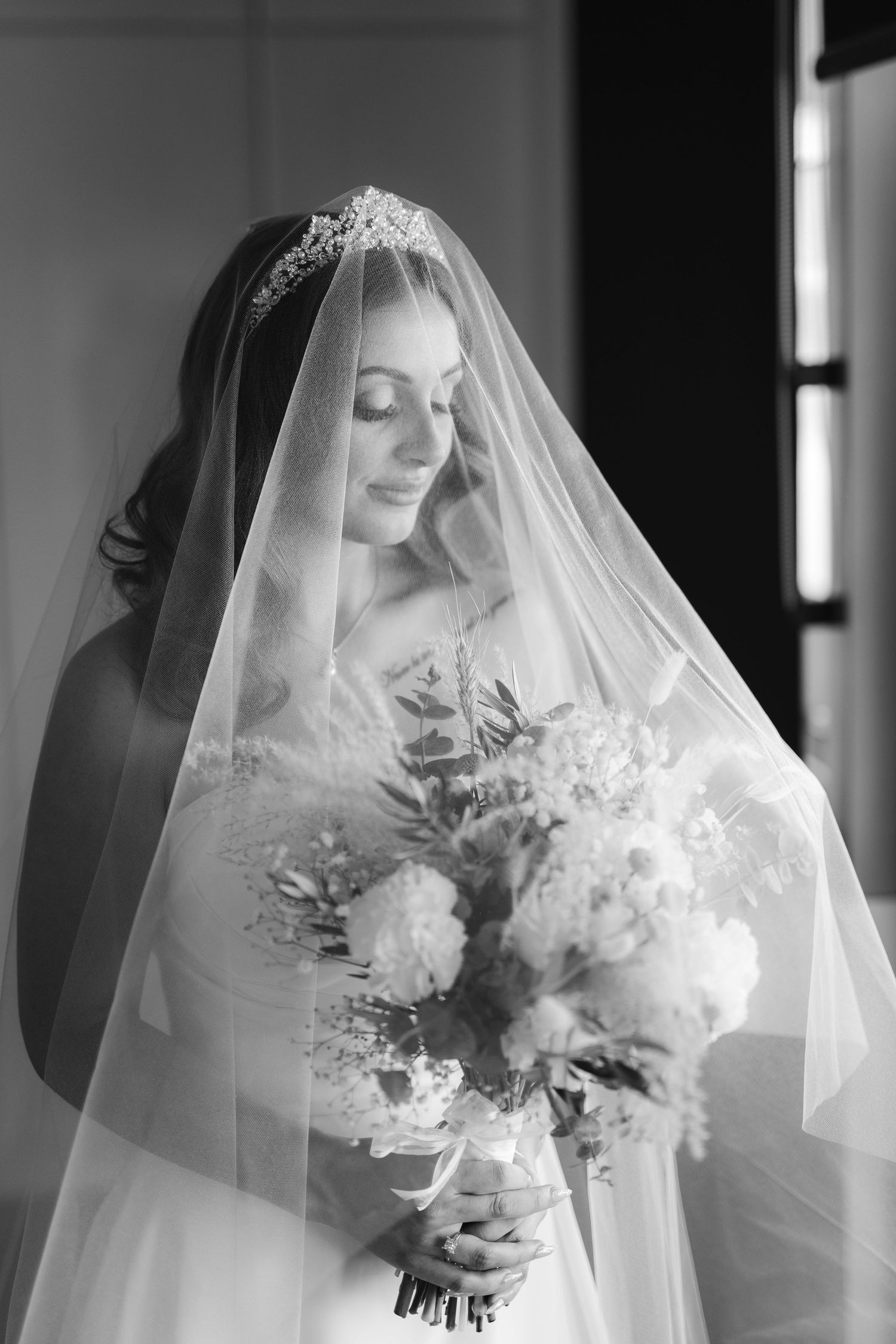 Black and white portrait of a bride in a delicate veil holding an elegant bouquet of white flowers on her wedding day.