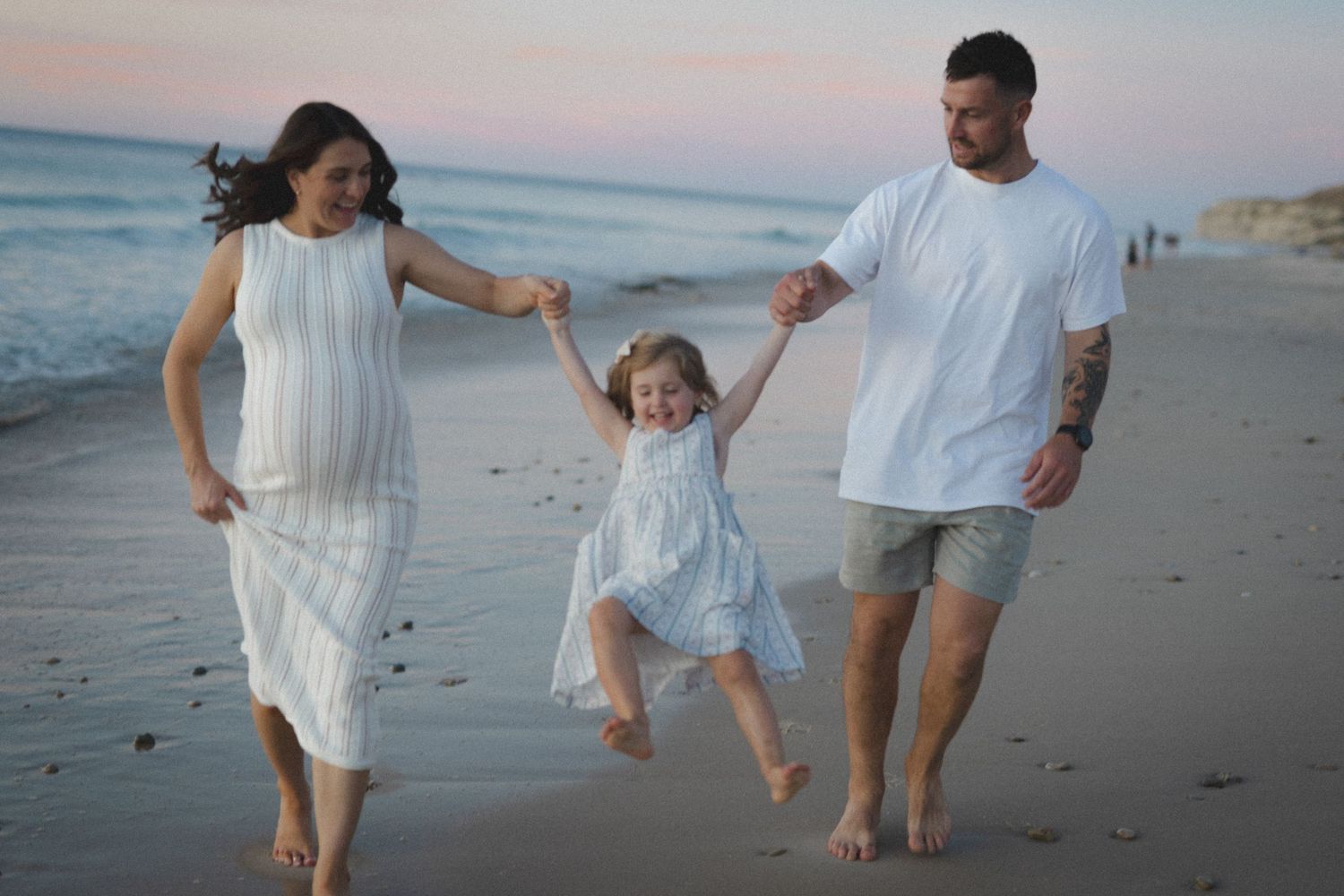 Family having fun lifting their child while walking on the beach at dusk.