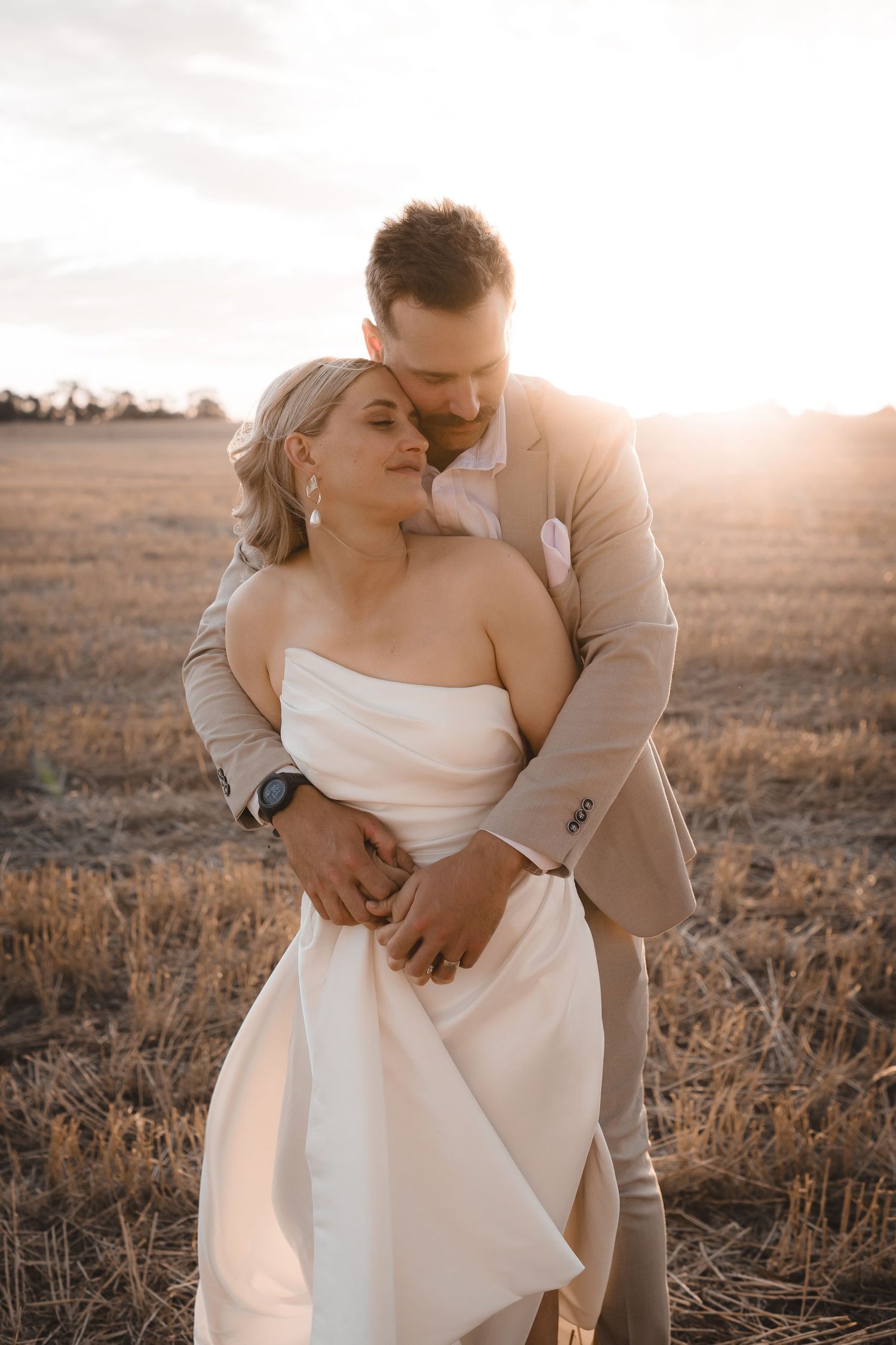 Intimate wedding portrait at golden hour in rustic field setting.