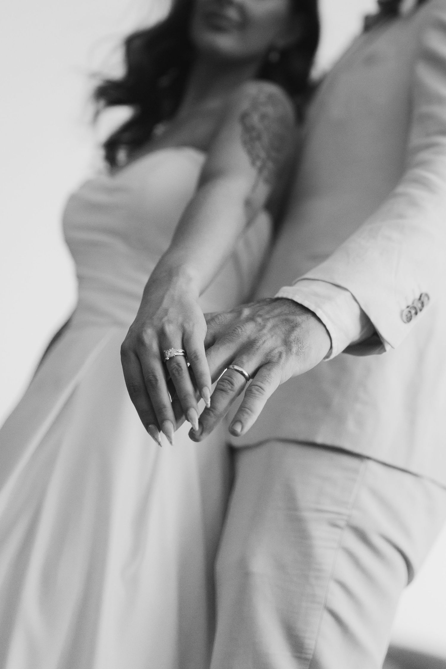 Black and white close-up of a couple's hands showing wedding rings in an intimate moment.