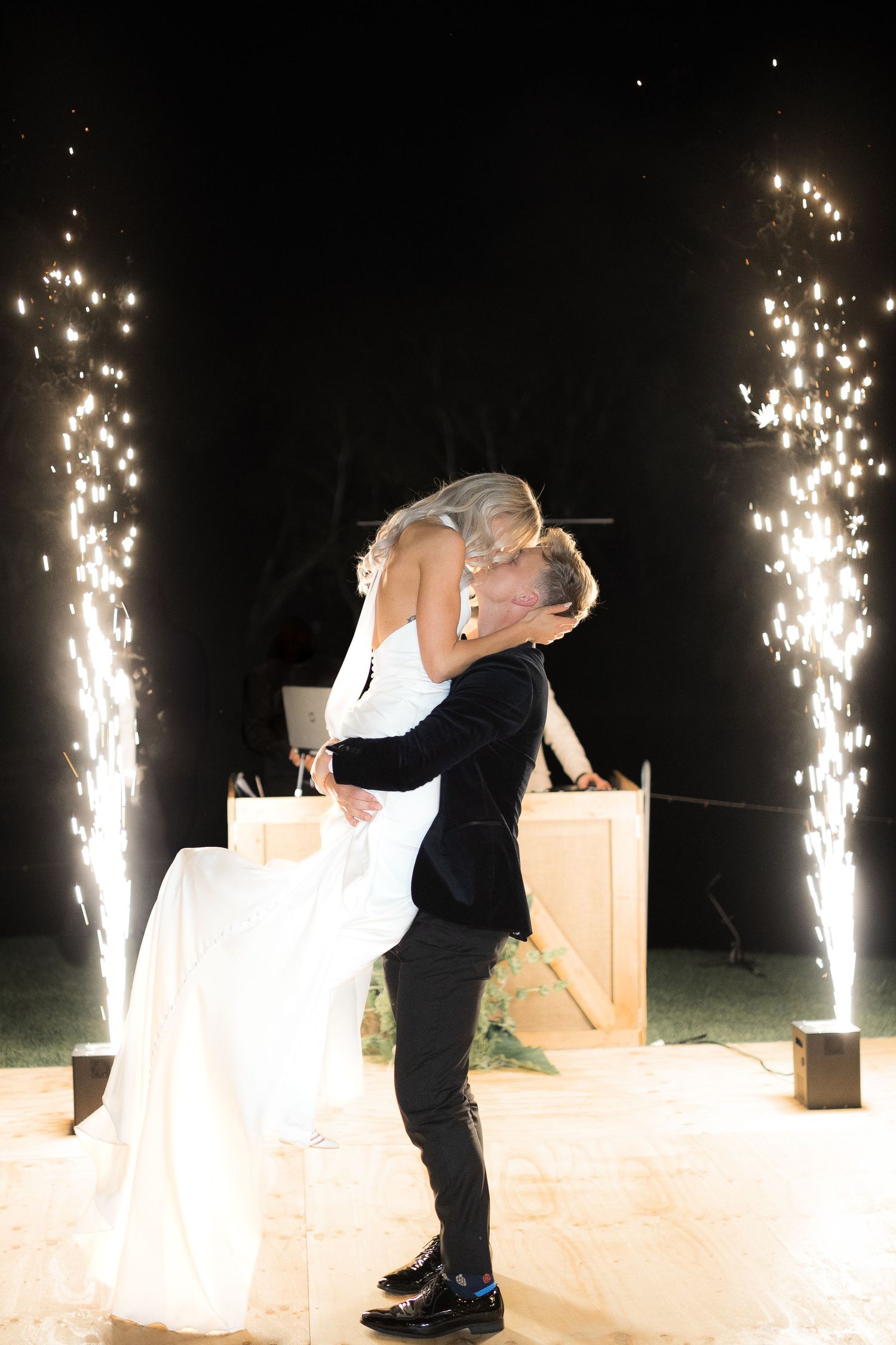 Newlyweds embrace in a dramatic kiss with sparklers creating a magical backdrop during their first dance.